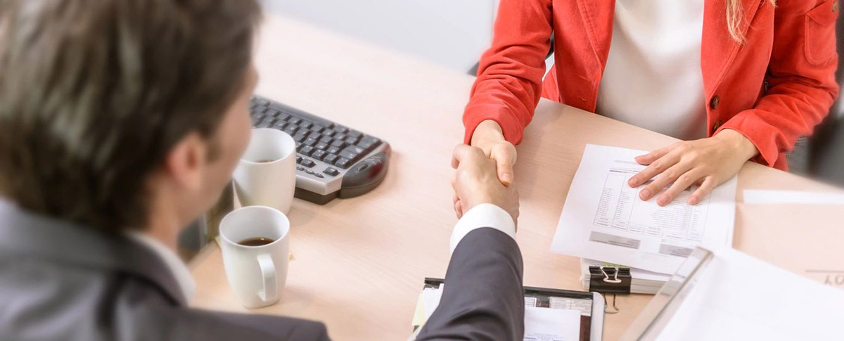 Two people shaking hands over a table with cups.