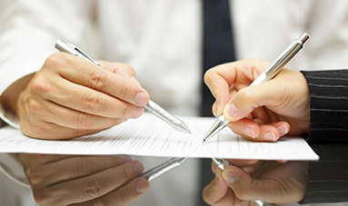 Two people are writing on a piece of paper.