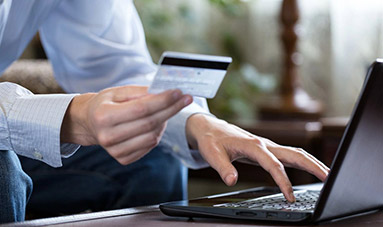 Young man using a laptop with credit card in other hand