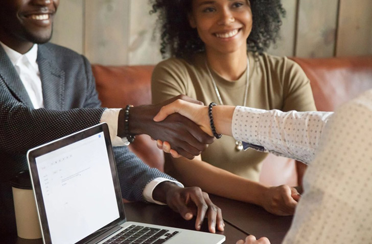 A woman shaking hands with another person over a laptop.